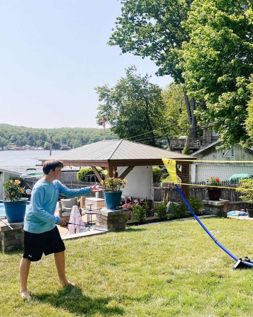 An enthusiastic young boy actively playing badminton in a vibrant, grassy backyard, skillfully swinging the racket towards the shuttlecock, illustrating the lively spirit of outdoor games.